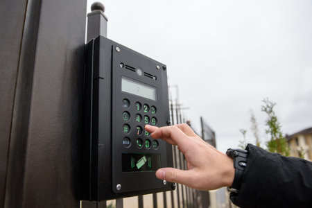 A person's hand reaches for an intercom with camera installed on a street fence. Close up, copy space.の写真素材