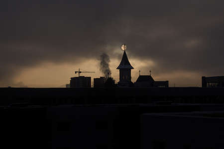 Fade sunrise with fog and dark sky with silhouette church and buildings  and sun behind the buildingsの写真素材