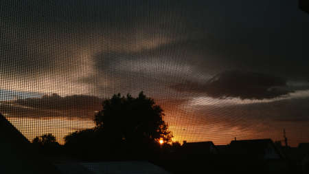 Fire sunset with backlit house and trees through a gridの写真素材