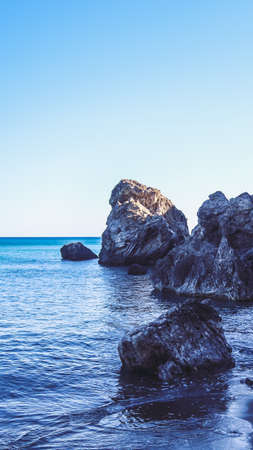 Seashore near a mountain with rocks and small wavesの写真素材