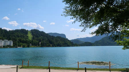 View of lake Bled in Slovenia, walking path and surrounding mountains during a sunny dayの写真素材