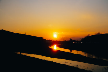 Intense orange sunset reflecting in the water of the curving river with clouds and copyspaceの写真素材