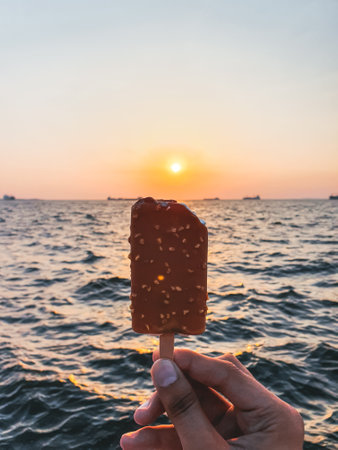 Hand holding an ice cream with the Aegean Sea in the background during sunset, Izmir, Turkeyの写真素材