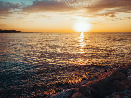 Sunset at Marmara Sea in Yalova city, Turkey. Cloudy weather. water hits red rocks in the foregroundの写真素材