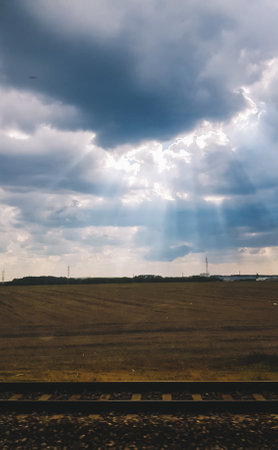 Cloudy sky with sunrays and railway tracks on the fieldsの写真素材