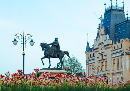 The statue of Stephen the Great and the Palace of Culture in IaÈi, Romania, framed by vibrant tulips in a picturesque springtime setting.の写真素材