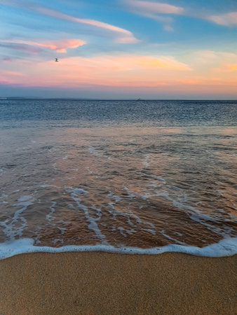 A peaceful sunset at a beach, with soft waves, golden sand, and pastel skies reflecting on the oceanの写真素材
