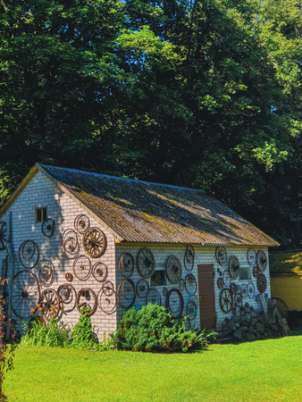 Old wagon wheels decorate a brick outbuilding set in lush greenery, with sunlight filtering through the surrounding forest in Renavas, Lithuaniaの写真素材