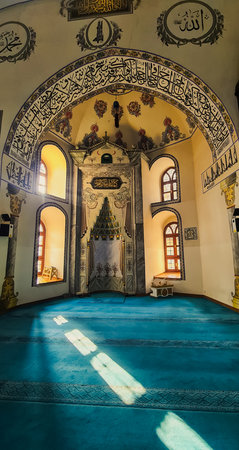 Sunlight streams onto the blue carpet of a beautifully decorated mosque interior with ornate...