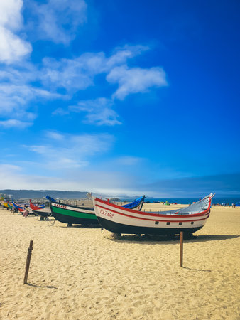 Nazare, Portugal, 24th of August 2024 - Colorful traditional fishing boats moored on sandy NazarÃ© beach in Portugal with blue sky and Atlantic Oceanのeditorial素材