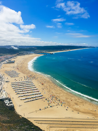 Aerial view of NazarÃ© beach with orange-roofed coastal town, golden sand, turquoise Atlantic waters and umbrellasの写真素材