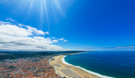 Aerial view of NazarÃ© beach with orange-roofed coastal town, golden sand, turquoise Atlantic waters and umbrellasの写真素材