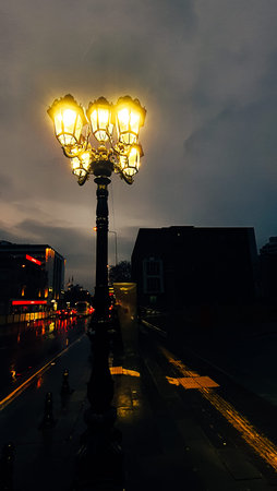 Ornate vintage street lamp glowing at night on a rainy city sidewalk with reflected lights on the wet pavementの写真素材