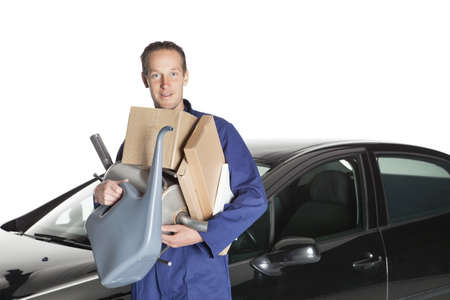 Portrait of confident worker with handful of mechanic stuff in front of car over white backgroundの写真素材