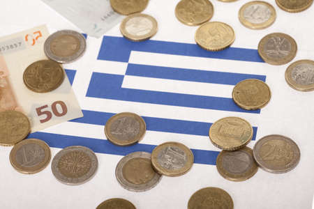 Few euro coins and paper currency on Greek flag indicating recessionの写真素材