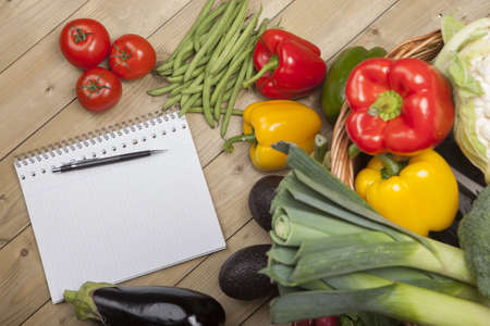 Open book ready for writing recipe with vegetables and basket on wooden surfaceの写真素材