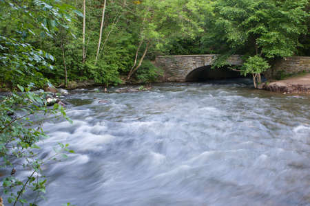 Rushing water of a creek goes under the arch bridge.