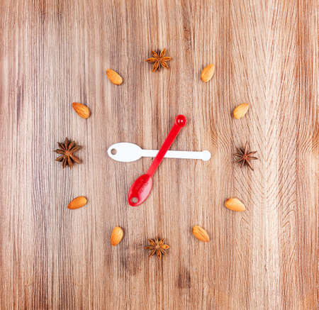 Clock face on a wooden background of almonds and star anise with arrow of measuring spoonsの写真素材
