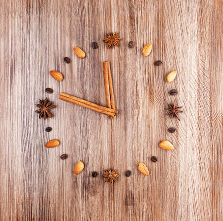 Clock face on a wooden background of almonds and coffee beans with arrow of cinnamon sticksの写真素材
