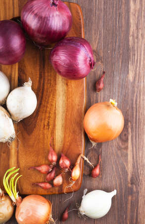 Different varieties of onions on a kitchen board and wooden surfaceの写真素材