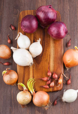 Different varieties of onions on a kitchen board and wooden surfaceの写真素材