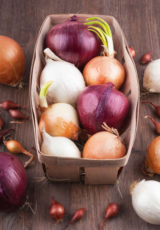 Different varieties of onions on a kitchen board and wooden surfaceの写真素材