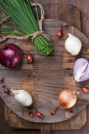 Different varieties of onions on a round kitchen board and wooden surfaceの写真素材