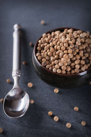 White pepper with metal spoon on black slate