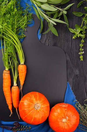 Carrots, pumpkin, sage, basil and thyme on a blackboard and a blue towel top view with copy spaceの写真素材