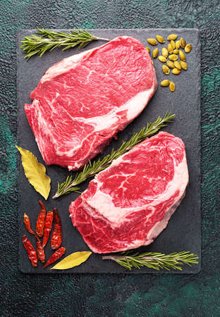 Two pieces of raw meat beef on a slate plate with rosemary