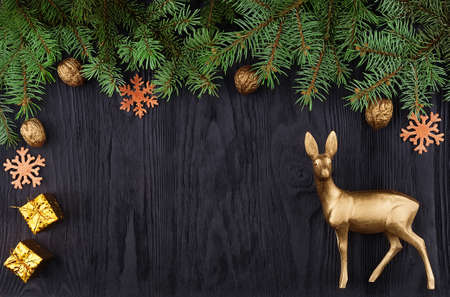 Christmas frame with spruce branches and a golden deer on a black wooden texture with copy spaceの写真素材