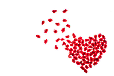 blowing heart shape made by pomegranate seeds isolated on whiteの写真素材