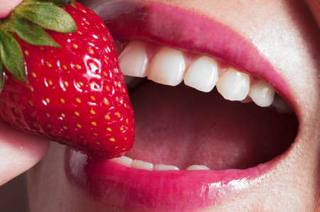 Macro close up of a beautiful female mouth eating a fresh strawberryの写真素材
