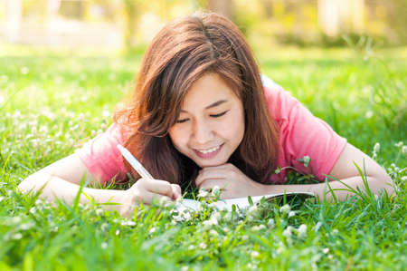 Happy Young Asian Woman Writing in Notebook and Smiling in Spring Garden.の写真素材