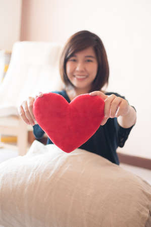 Young asian woman hold red heart soft toy.の写真素材