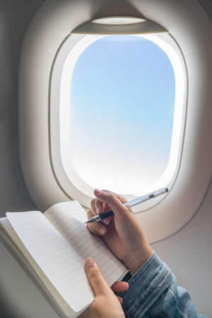 Woman writing on blank notebook while travelling on airplane.の写真素材