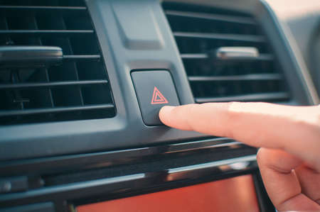 Woman finger pressing emergency button on car dashboard
