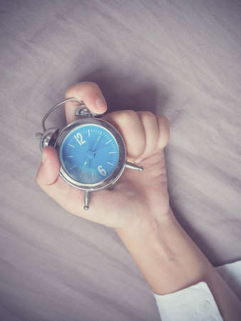 Hand grabing alarm clock on bed backgroundの写真素材
