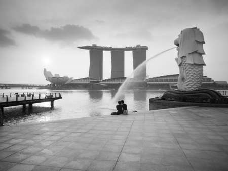 SINGAPORE - MARCH 10, 2013: Couple sitting relax in the morning at Merlion Park, Marina Bay. Merlion is a mythical creature with the head of a lion and the body of a fish is a symbol of Singapore.のeditorial素材