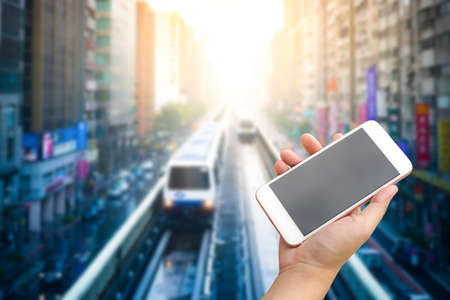 Smartphone on hand with train trought city building background.の写真素材