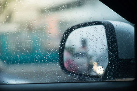 Blurred view of road traffic in rainy day with rain drop on car side view mirror