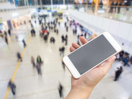 Hand holding smart phone with passengers inside transit station of subway background