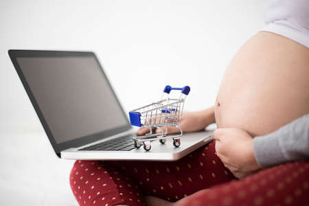 Pregnant woman using laptop notebook computer with shopping cartの写真素材