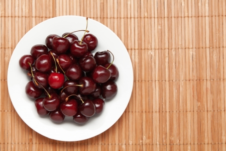Sweet cherry on a white dish. Dish on a wooden cloth.の写真素材