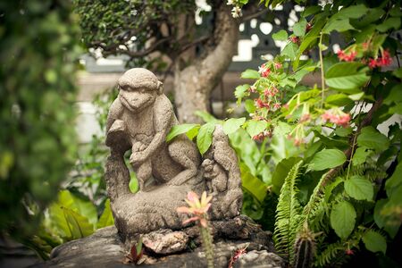 The stone figurine of a monkey is surrounded by greens and colorsの写真素材