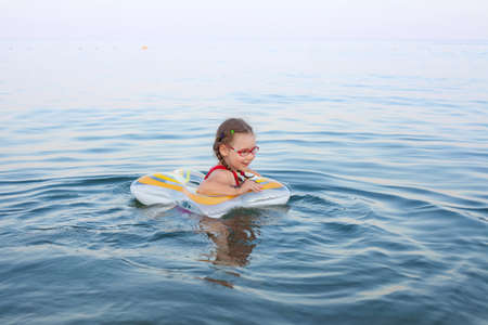 young beautiful girl in a red swimsuit swims on a rubber ring on the sea