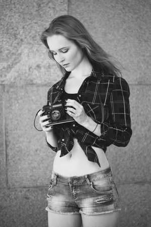Girl in shorts and a red shirt in a cage, with a retro camera in her handsの写真素材