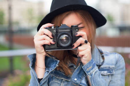 Young girl photographer walking along the street in a jeans jacket with an old cameraの写真素材