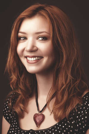 portrait of the young beautiful girl with red hair, in a black dress, on a dark background
