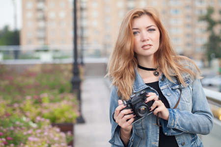 Young girl photographer walking along the street in a jeans jacket with an old cameraの写真素材